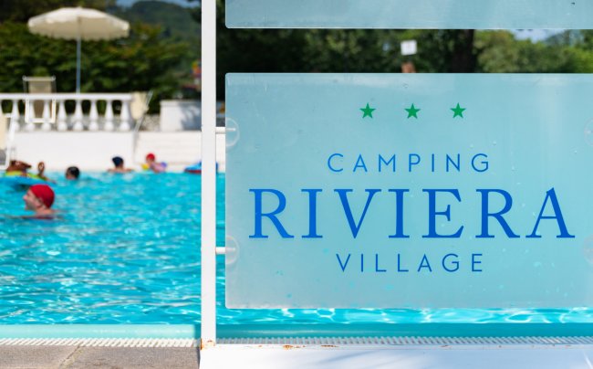 Piscina con persone che nuotano, visibile il cartello 