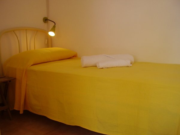 Letto singolo con copriletto giallo, lampada da lettura e asciugamani bianchi piegati.