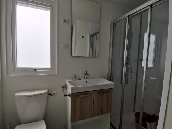 Bagno compatto con doccia, WC, lavandino con mobile in legno e specchio.