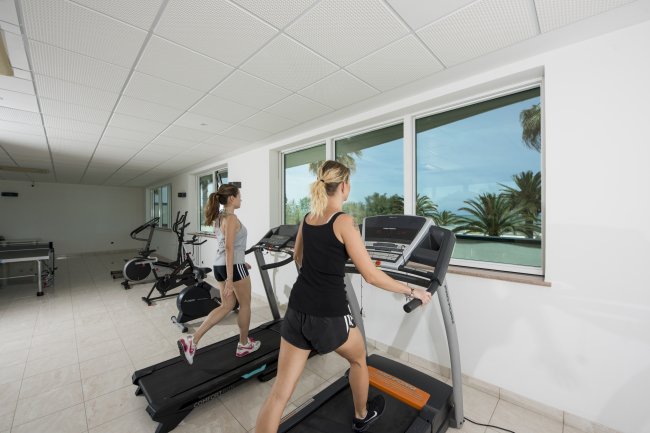 Due persone su tapis roulant in una palestra luminosa con finestre.