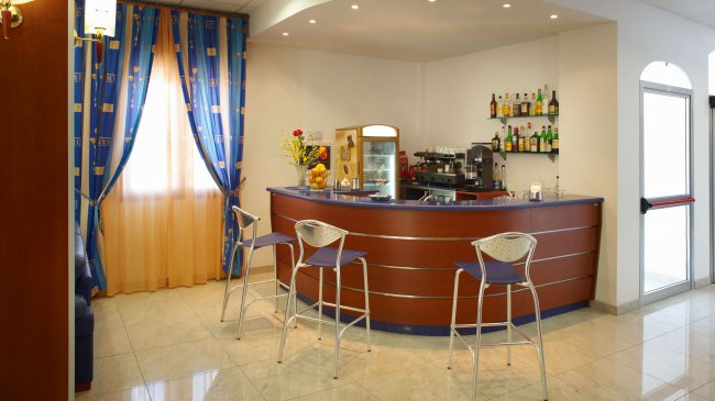 Bar d'albergo con bancone curvo, sedie alte e alcolici esposti.