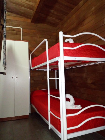 Cameretta con letti a castello rossi e armadio bianco, pareti in legno.