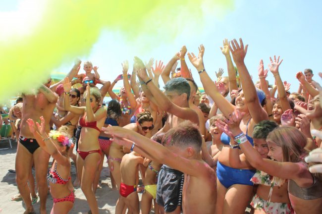 Gruppo di persone in costume da bagno con braccia alzate e polvere colorata gialla nell'aria.