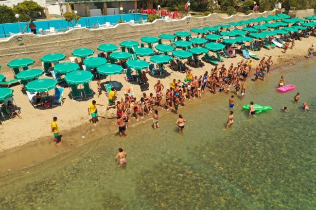 Spiaggia affollata con ombrelloni verdi, persone sulla sabbia e in acqua.