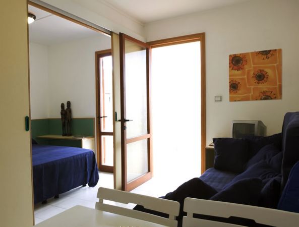 Un soggiorno con divano scuro, tavolo da pranzo e porta finestra che separa la camera da letto.