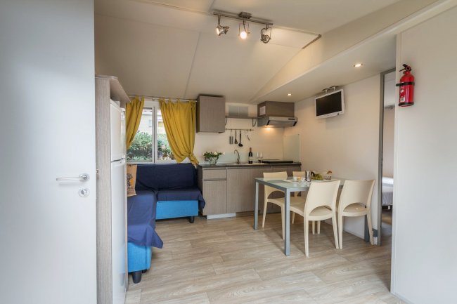 Interno di un soggiorno con cucina, tavolo da pranzo, divano blu e tende gialle.