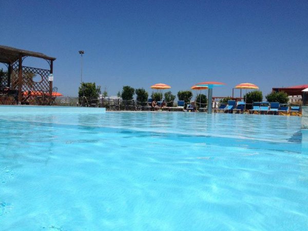 Piscina all'aperto con ombrelloni colorati sotto un cielo blu.