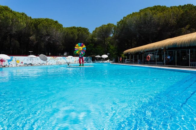 Vista della piscina con una decorazione colorata al centro e una tettoia di paglia a destra.