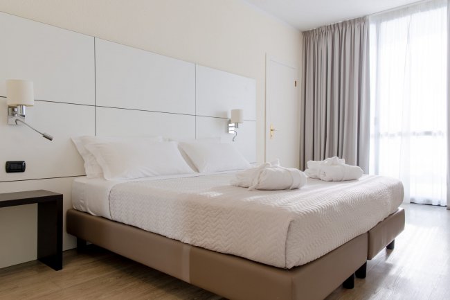 Letto matrimoniale con lenzuola bianche, due accappatoi, e applique bianche su testiera.