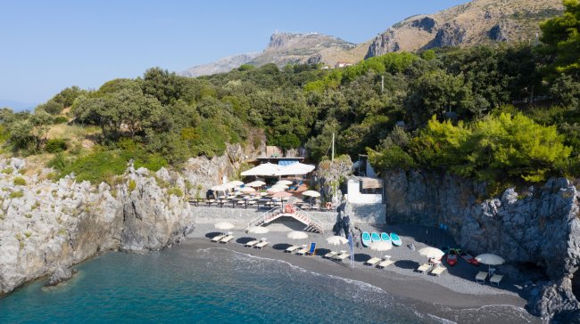 Spiaggia rocciosa con ombrelloni e lettini.
