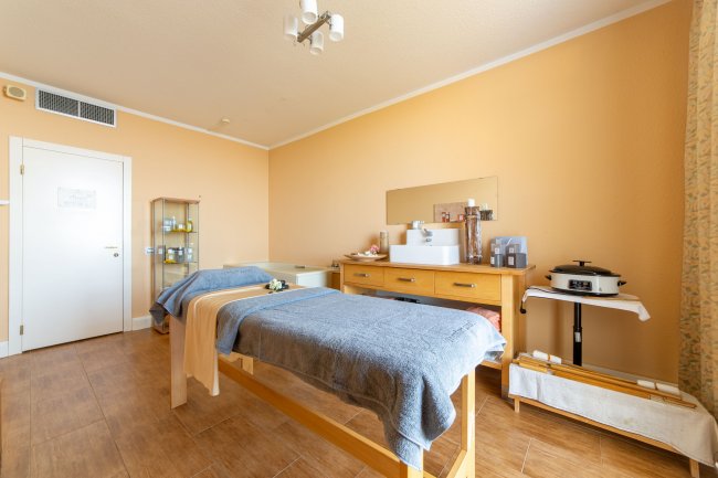 Sala massaggi con pareti colore pesca, due lettini coperti da teli blu e mobili in legno chiaro.