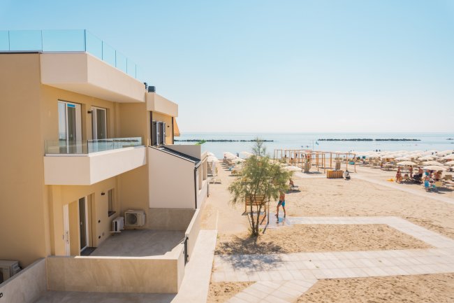 Una spiaggia con ombrelloni e sdraio, vista da un edificio con balconi.