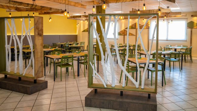 Sala da pranzo con sedie verdi, divisa da pannelli decorativi.