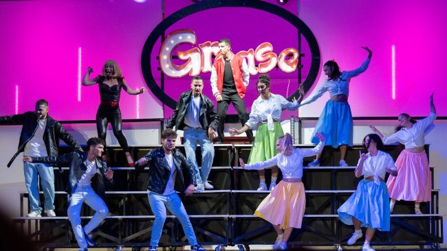 Performance teatrale di Grease con costumi anni '50 su un palco.