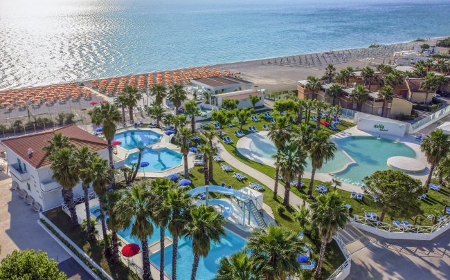 Resort con piscine e palme vicino alla spiaggia, mare scintillante.