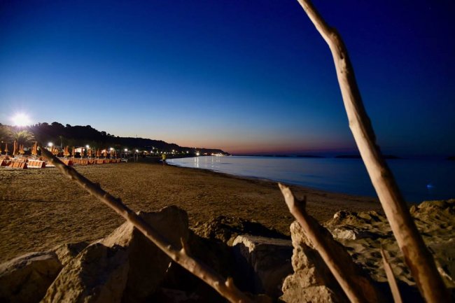 Spiaggia al tramonto con cielo blu scuro e luci accese sul lungomare.