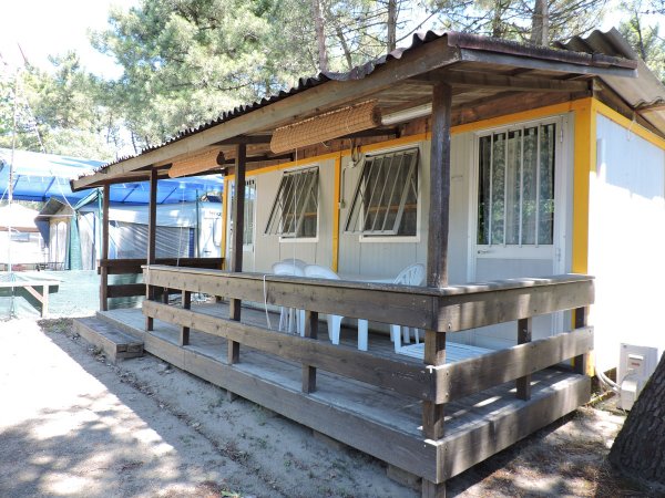 Una casetta di legno con veranda e sedie bianche, situata tra gli alberi.