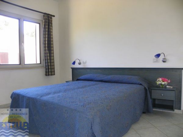 Una stanza d'albergo con letto matrimoniale coperto da una trapunta blu e una finestra.