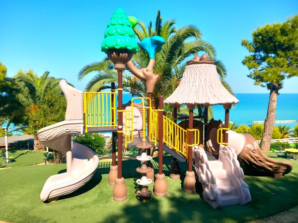 Un parco giochi con scivoli beige vicino al mare e palme.