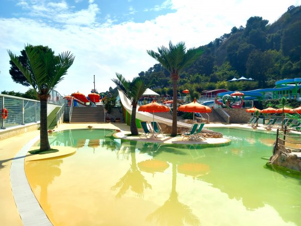 Piscina con scivoli bianchi, ombrelloni arancioni e palme.