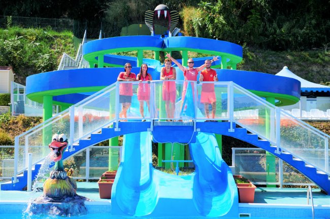 Cinque persone in divisa rossa posano sopra uno scivolo acquatico blu con decorazioni colorate.