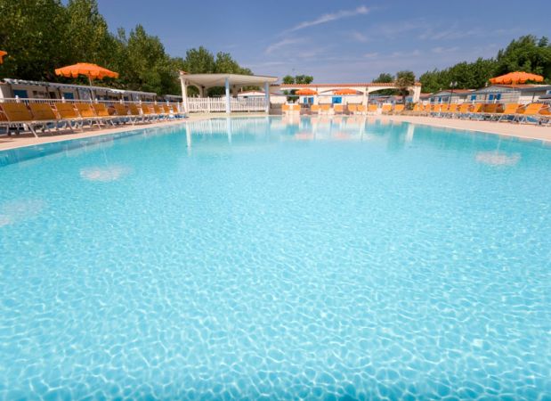 Piscina vuota con sdraio e ombrelloni sullo sfondo.