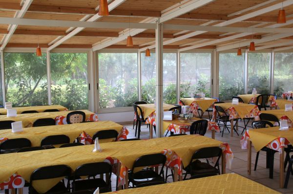 Una sala da pranzo con tovaglie gialle e sedie nere, circondata da finestre.