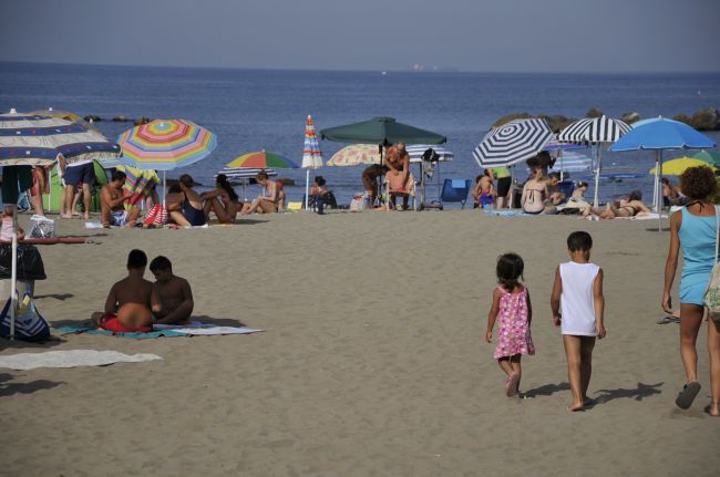Una spiaggia affollata con persone sotto ombrelloni colorati vicino al mare.