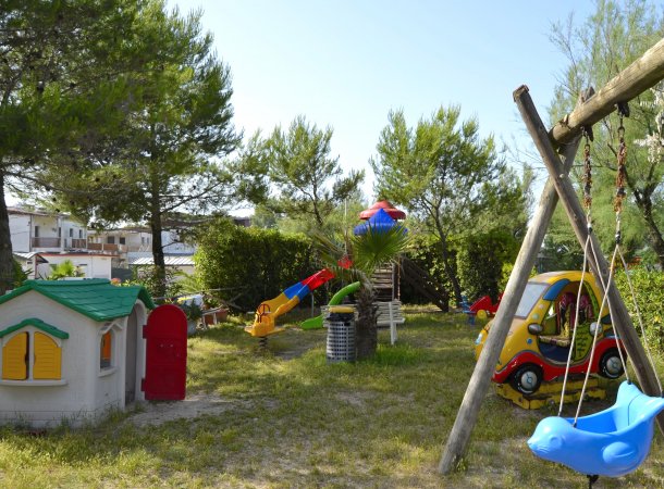 Parco giochi con altalene, scivoli, una casetta in miniatura e un'automobile giocattolo colorata.